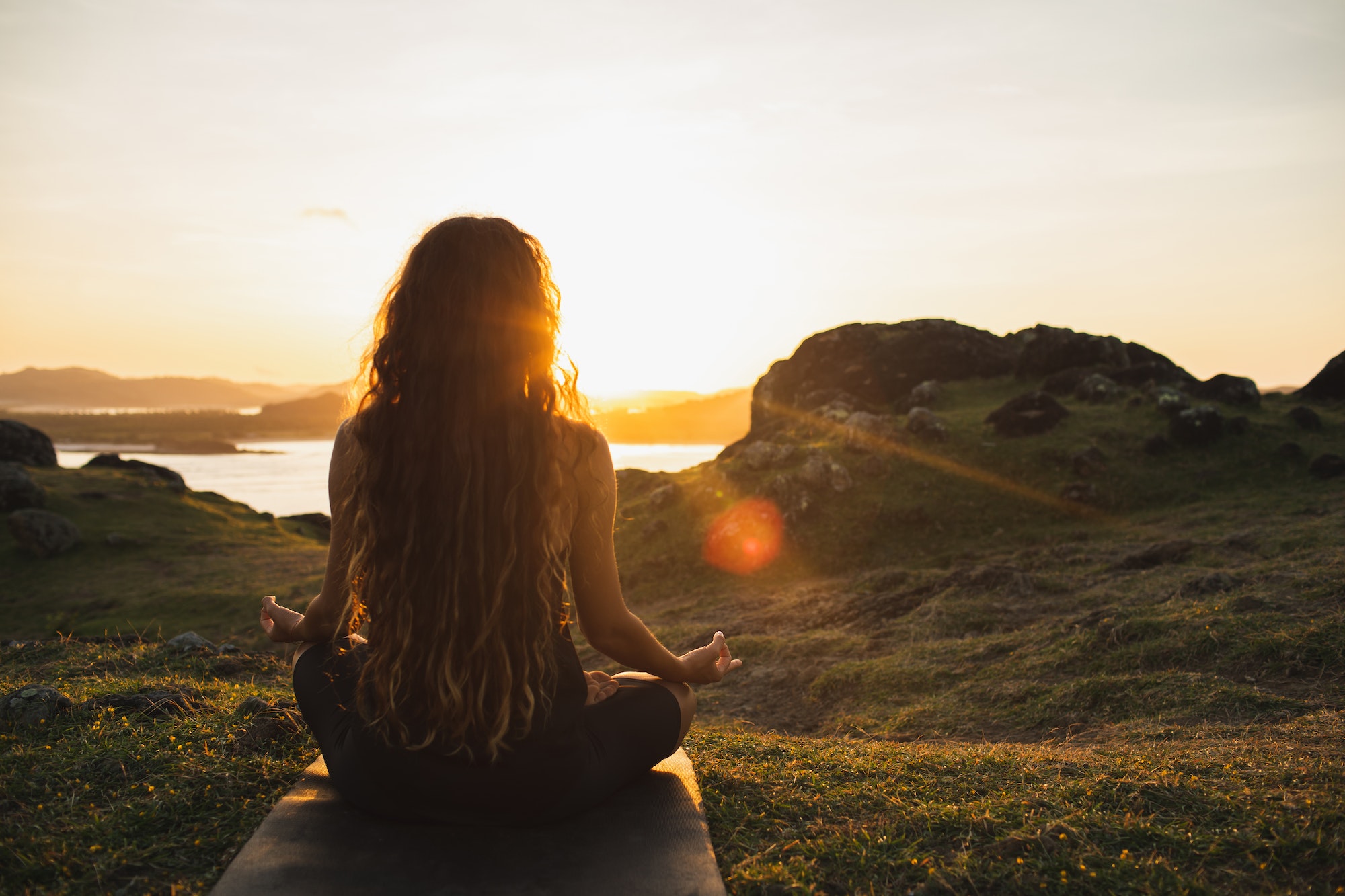 Woman meditating yoga alone at sunrise mountains. View from behind. 